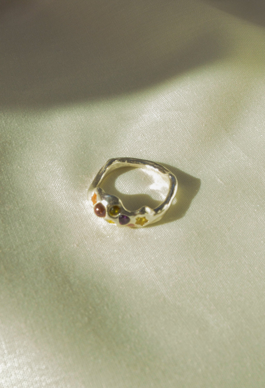 Silver ring with colorful stones on a light green fabric background