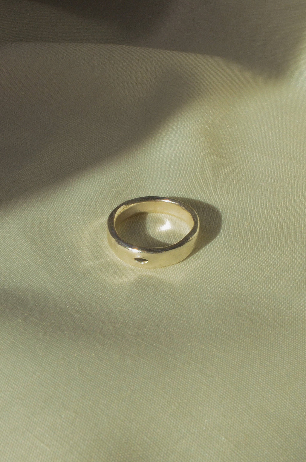 Silver ring on a textured beige surface with soft shadows