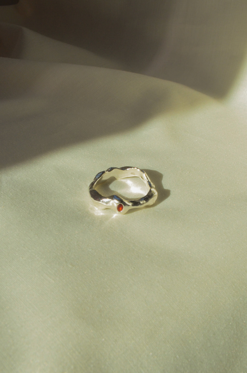 Silver ring with a red gemstone on a light green fabric background