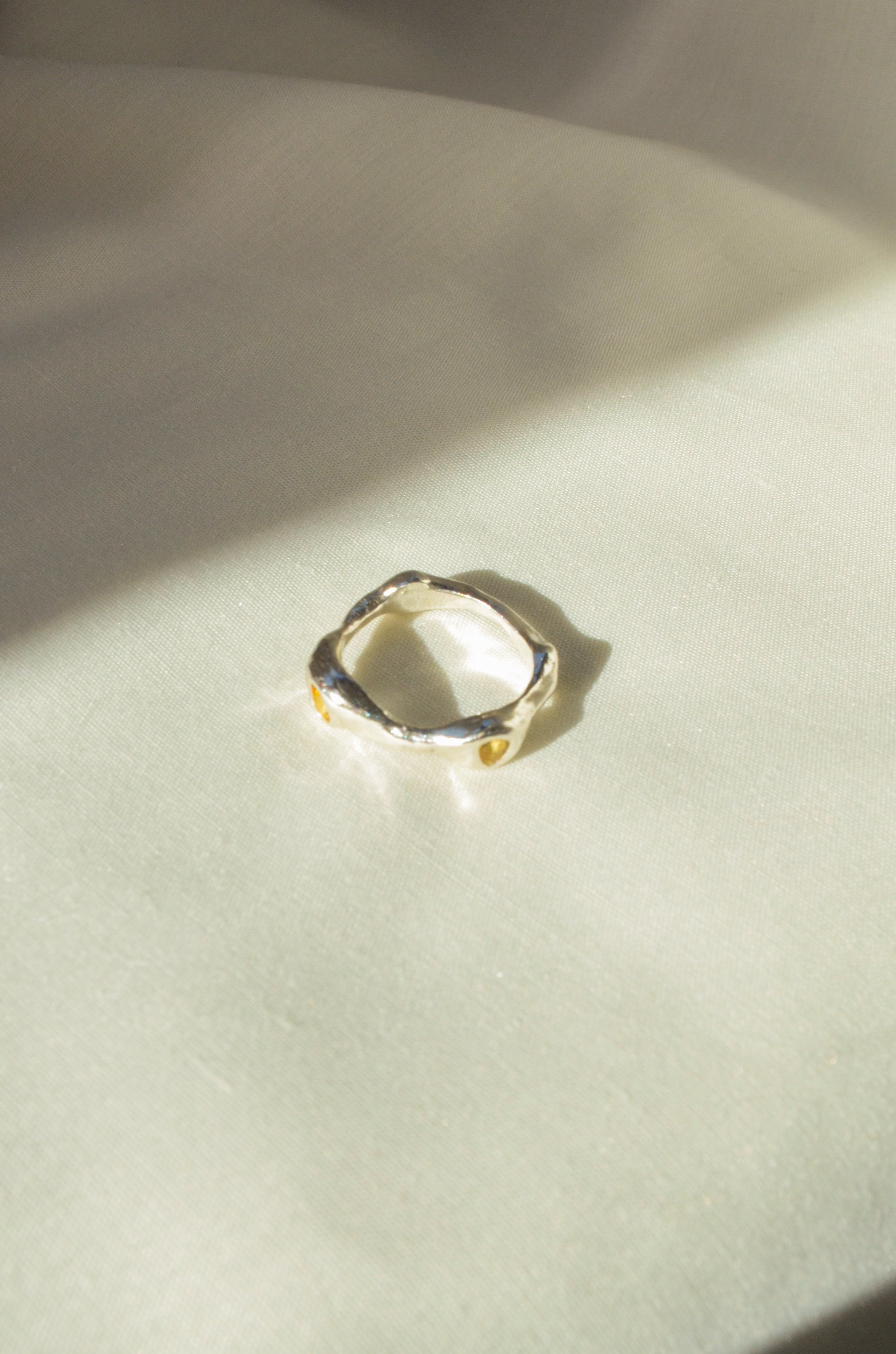 Silver ring on a textured beige surface with soft shadows