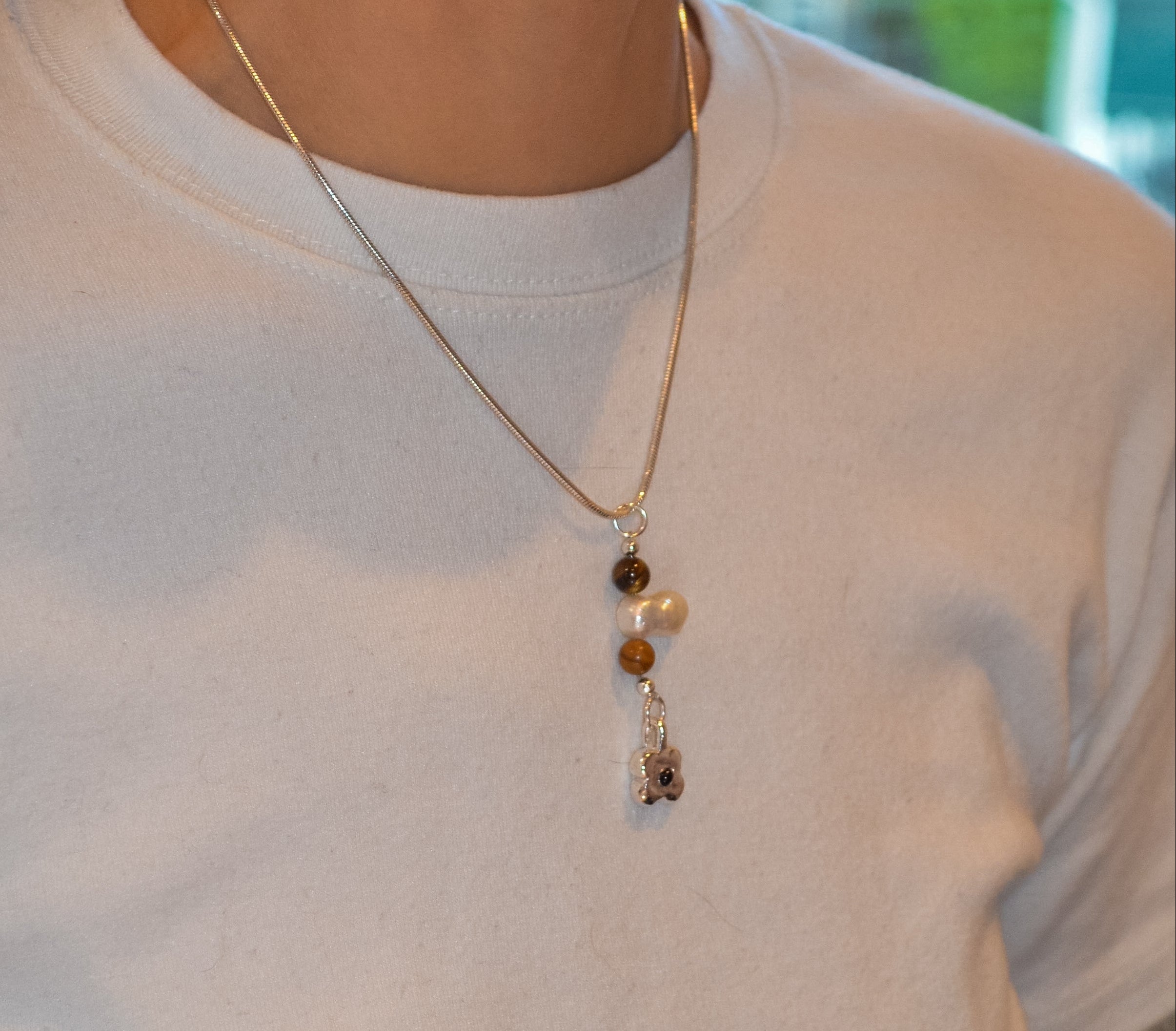 Person wearing a necklace with a pendant on a plain background
